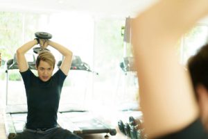 A person lifting a dumbbell overhead for a triceps extension.